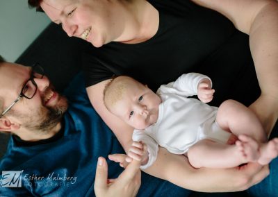 Baby meisje trekt een serieus gezicht tijdens de lifestyle fotoreportage, terwijl haar ouders elkaar vrolijk aankijken
